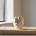 Hand-finished plaster vessel on raw travertine surface in morning gallery light
